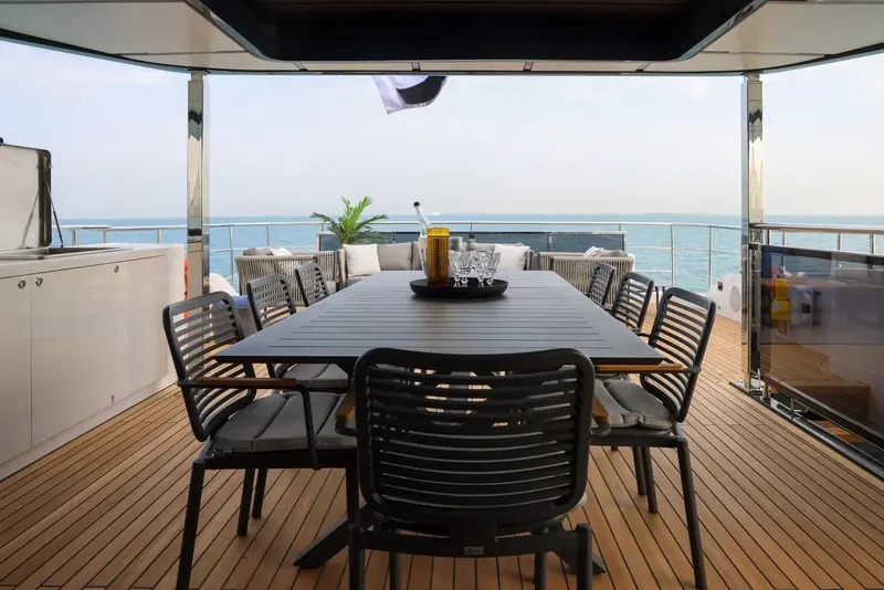 An aft-deck dining table under the flybridge overhang gives a sheltered outdoor alternative to the interior dining room.