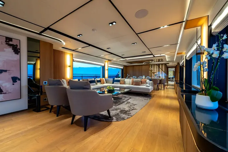 The main-deck lounge runs the full beam in warm wood tones, with a separate seating area kept distinct from the formal dining space forward.