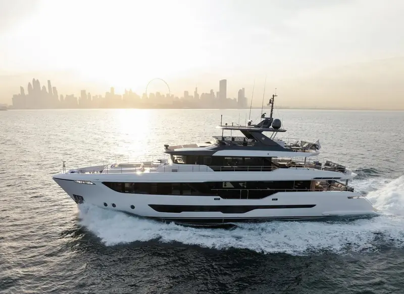 Under way bow-on into the same golden light, the flybridge hardtop and the terrace balconies folded flush into the hull side visible in profile.