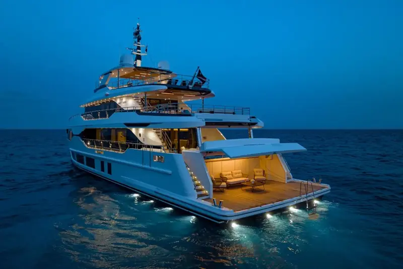 At anchor after dark with the transom beach club open and lit. The drop-down bulwark section and the underwater lighting are standard on every Majesty 120 delivered so far, Yoto included.