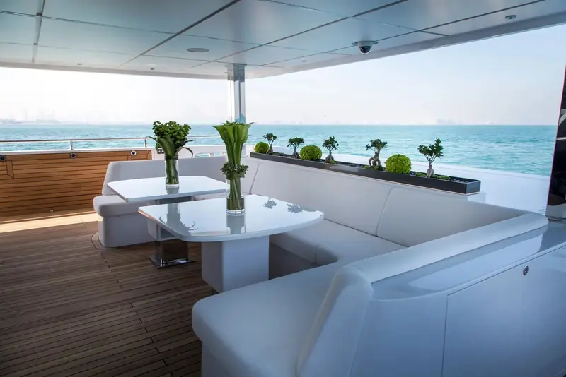 An aft-deck dining table sits under the overhang of the deck above, sheltered from sun while keeping a clear view out over the transom.