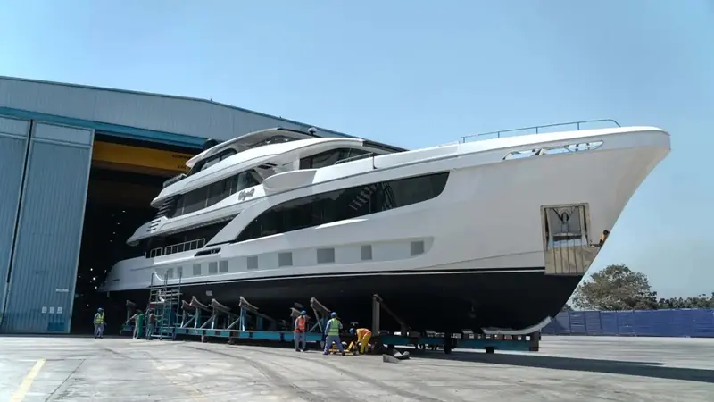 The first Majesty 145 rolls out of Gulf Craft's UAE build shed on its transporter cradle, her cursive nameplate below the sheer line as workers guide the stern clear of the doors.
