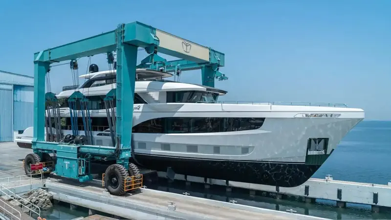 A second hull in a marbled grey livery held aloft by the travel lift at the quay, her name on the topsides ending in a lone Q.