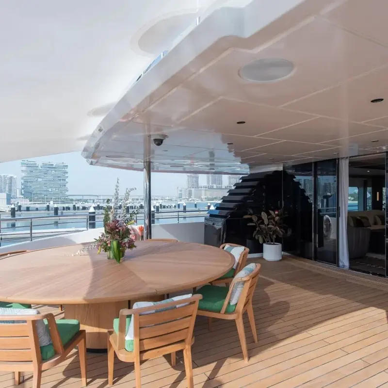 The upper-deck dining table sits under an open sky with the Dubai waterfront as backdrop, one of several outdoor entertaining zones spread across the boat's three decks.