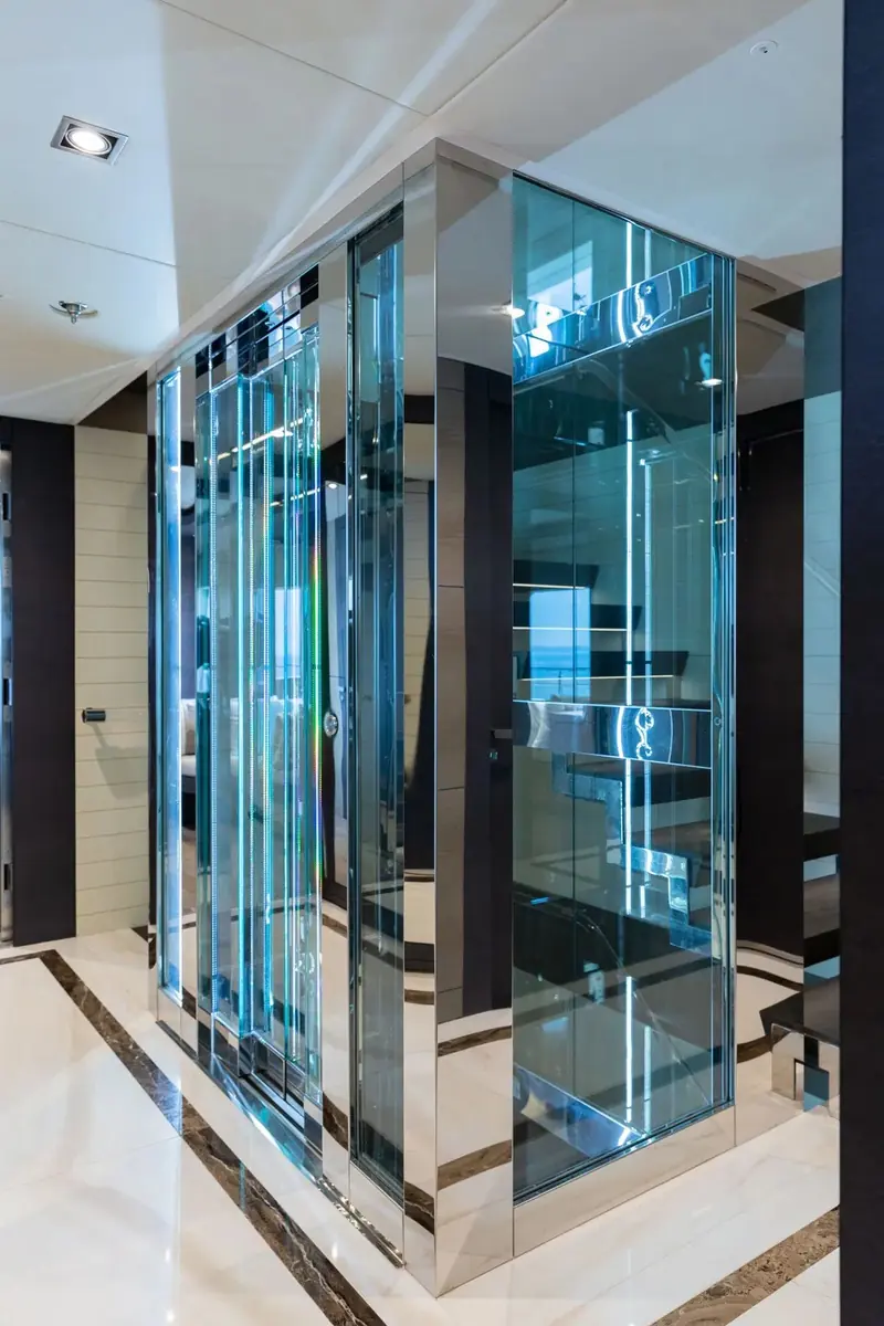 A glass-walled feature stairwell lit blue at night, part of the interior architecture Gulf Craft uses to distinguish the 175 from its own smaller Majesty models.