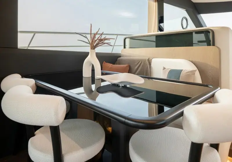 A dining nook with a ceramic vase centrepiece, seating arranged around a glass-topped table beneath the flybridge overhang.