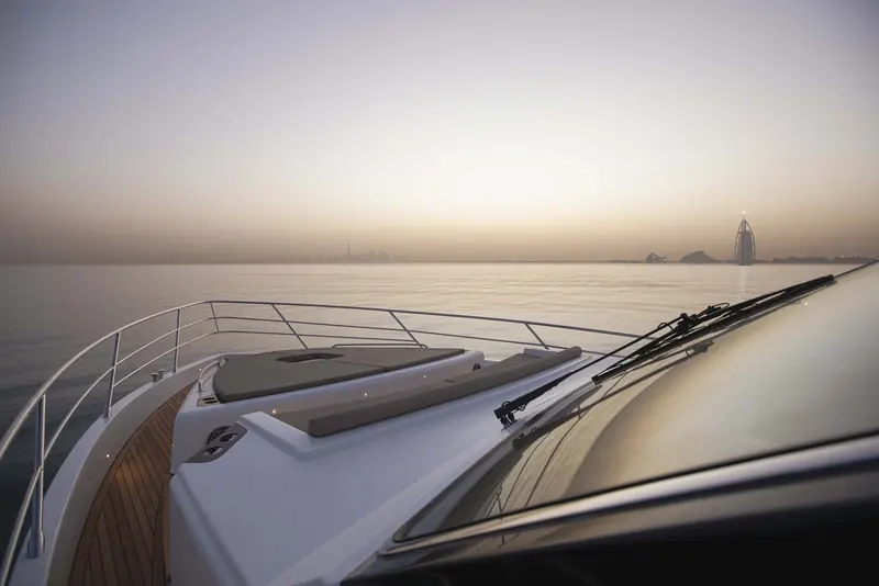 A bow-rail detail at sunset with the Burj Al Arab in the distance, showing the foredeck sunpad that doubles as the boat's forward lounge.