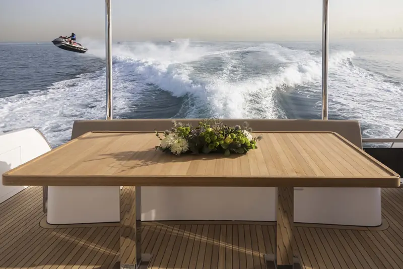 The aft cockpit dining table sits low over the swim platform, with a jet ski trailing the wake behind, the kind of day-boat use the 62 is bought for.