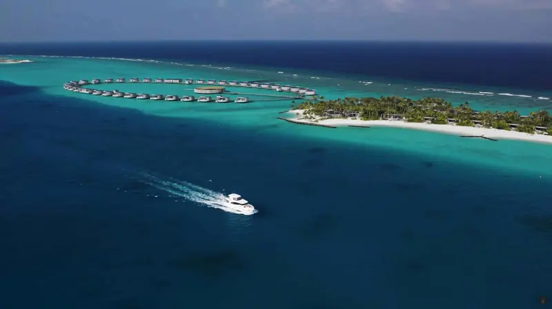 Seen from the air against a Maldivian atoll, the boat's compact footprint next to the resort's own villas shows the scale a 62-footer actually offers.