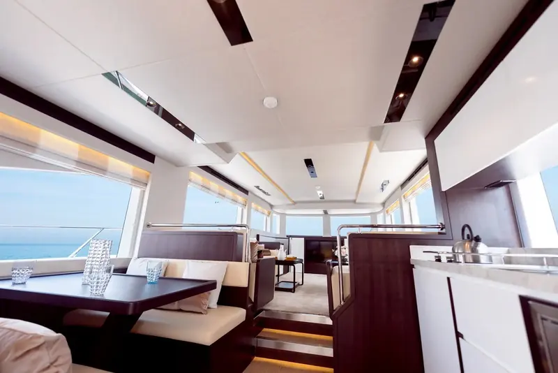The main-deck saloon and galley sit open-plan behind full-height windows, giving the helm and the dining table a shared sightline out to the water.