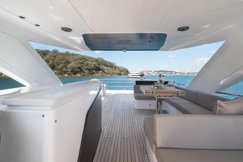 Flybridge lounge seating shot from the aft rail, city skyline visible over the transom and open water beyond.