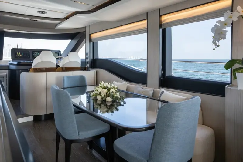 Main-deck dining table for six beside the helm, full-height windows on both sides putting the water at eye level from the seats.