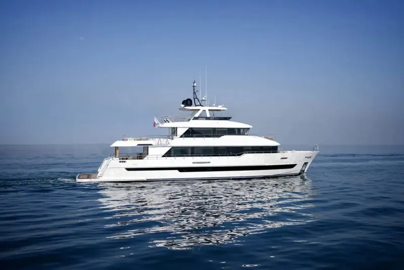 Nomad 101 at rest in flat calm water, her raked bow and full-length hull glazing shown in clean profile against a hazy city skyline.