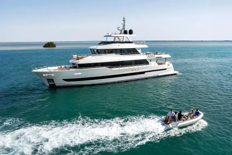 Under way alongside her own tender off a low green island, giving a real sense of scale against the smaller boat.