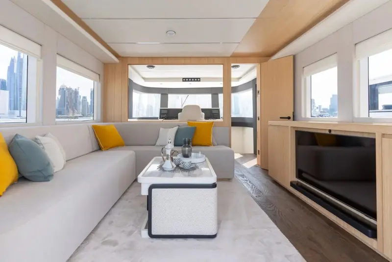The main-deck saloon looks forward past the entertainment cabinet, with the Gulf coast skyline through glass on both sides.
