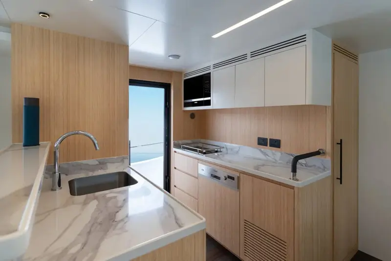 The galley, stone surfaces and a full hob against the outboard side. The 2027 boat adds a separate crew galley so this one stays with the guests.