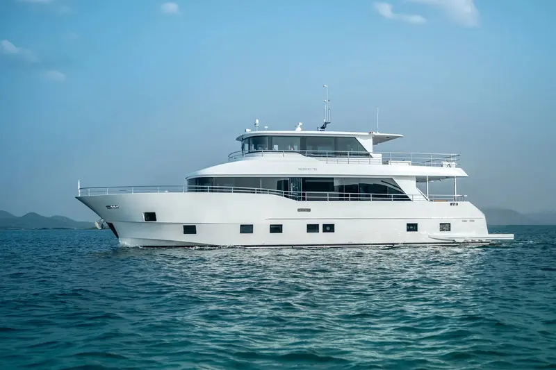 Nomad 75 at rest against low hills, her displacement-style hull and full-beam wheelhouse windows visible in profile.