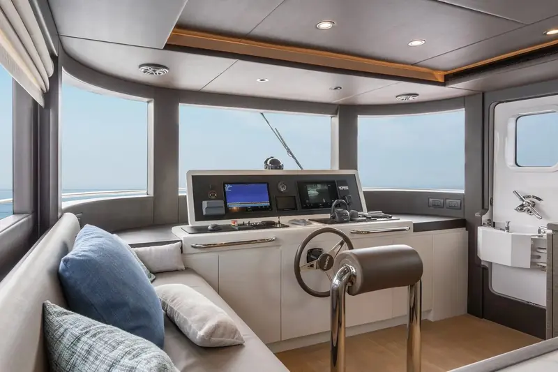 The wheelhouse settee and helm seen from the companionway, upholstered in pale grey with a full wraparound window line.