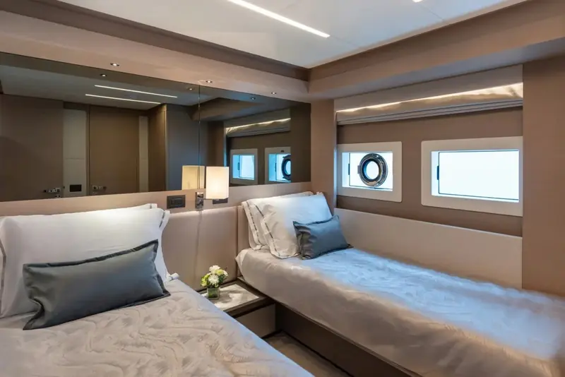 A twin-berth cabin finished in warm wood veneer, portholes rather than hull windows marking this as a lower-deck stateroom.