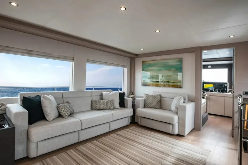 The main salon, sofa and window seating arranged around a low table with the sea visible on both sides through full-height glazing.