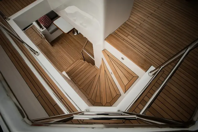 Looking straight down the internal stairwell from the flybridge to the lower deck, teak treads spiralling past a full-height window.