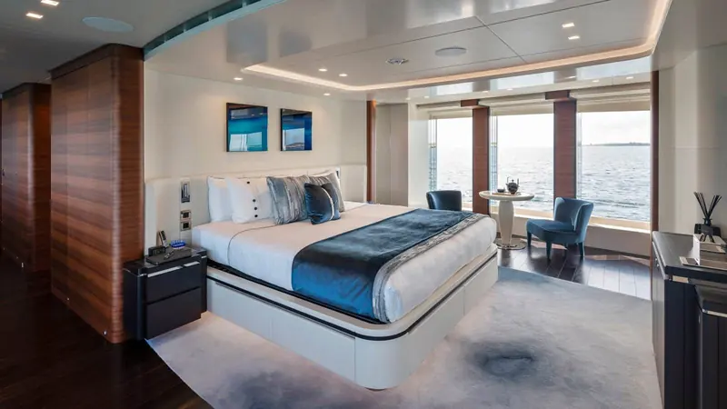 A guest stateroom finished in dark wood panelling with full-height windows, giving cabins below the main deck the same sea view usually reserved for the owner's suite.