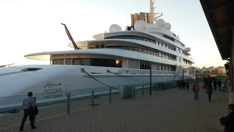 Azzam's bow at the quay, carrying both its Arabic and Latin nameplates - "Azzam" above "Abu Dhabi", its port of registry - with pedestrians giving a sense of true scale.