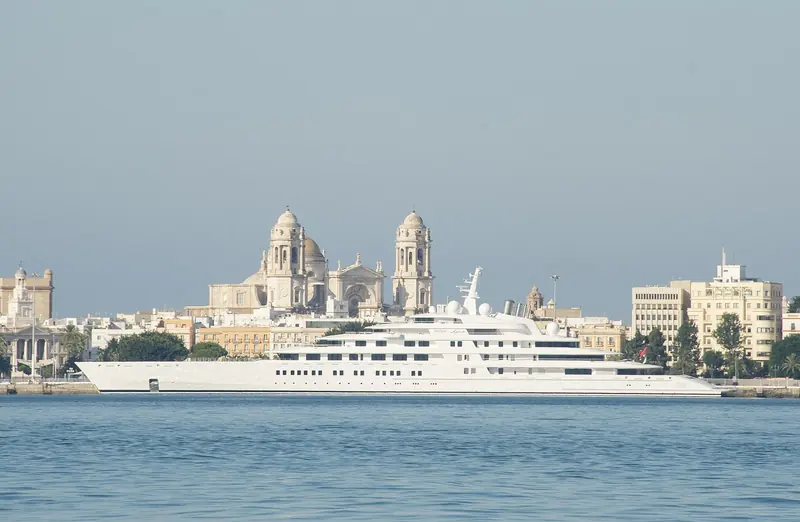Azzam passing Cadiz's baroque cathedral towers, her 180-metre hull dwarfing the historic waterfront behind it.