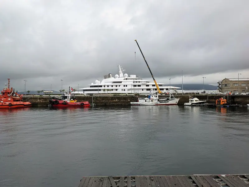 Azzam docked in Vigo, Spain under a working crane, her name visible on the hull between the aft superstructure decks.
