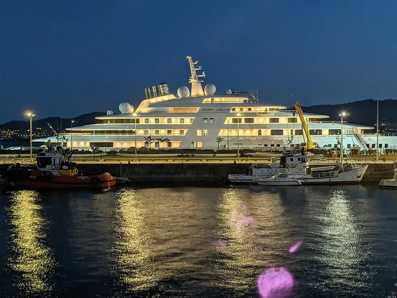 Azzam lit up at dusk in Vigo harbour, dwarfing the tugs and fishing boats moored alongside.