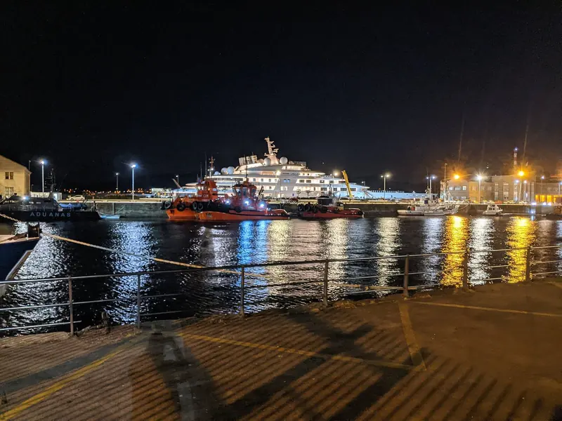 Azzam at night in Vigo, seen past customs and pilot boats on the quay - the scale of the hull only becomes clear against the working harbour craft in front of it.