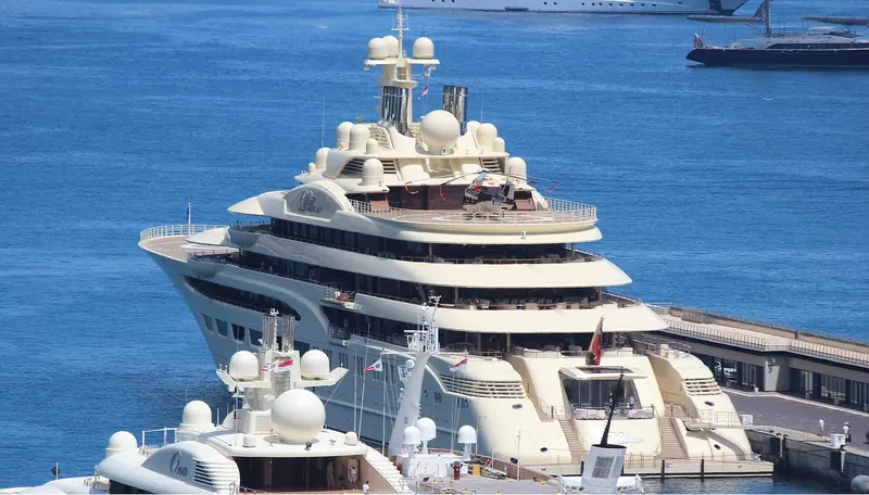Dilbar moored in Monaco harbour with a helicopter parked on its aft deck pad, next to the smaller Feadship Ona - the two hulls illustrate the size gap between a merely large superyacht and Lurssen's biggest build.