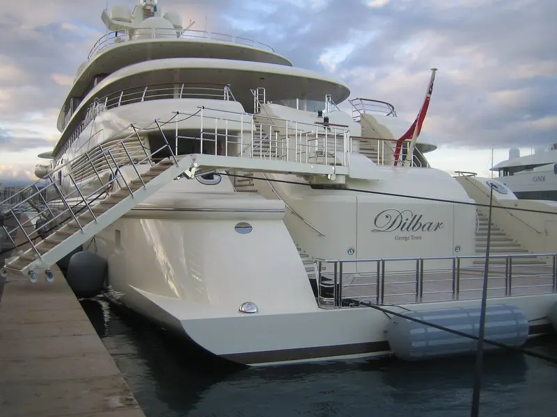 Dilbar stern-to at a marina berth, gangways down on both quarters, showing the sheer freeboard a 156-metre motor yacht carries even alongside the dock.
