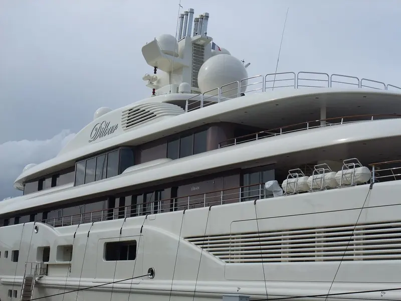 Dilbar's starboard profile at the quay, decks stacked above a hull line low enough to reveal how much of the yacht's volume sits above the waterline.