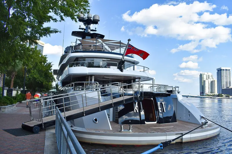 Kismet moored on the St. Johns River in Jacksonville, Florida, her stern tender ramp lowered to the dock and the city's downtown towers behind her.