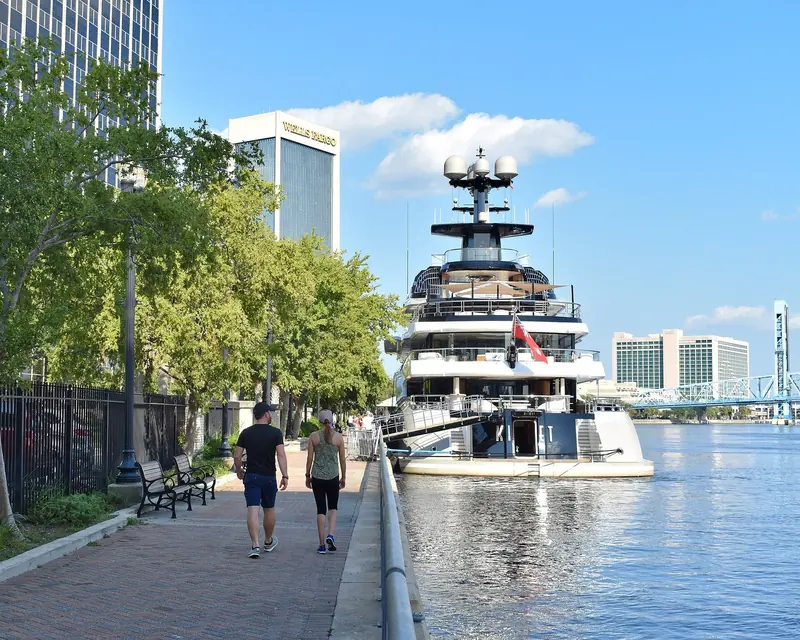 Passers-by on the Jacksonville riverwalk beside Kismet, whose scale next to the pedestrian path gives a sense of her true size.