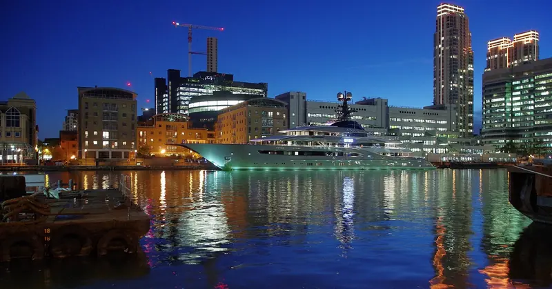 A wider night view of Kismet on the City Canal, Canary Wharf's towers reflected in the water beyond.