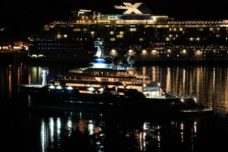 Lit up at night alongside a cruise ship for scale. Even berthed next to a vessel many times her tonnage, Octopus reads as the more purposeful shape - flatter decks, fewer curves, a working profile rather than a resort one.