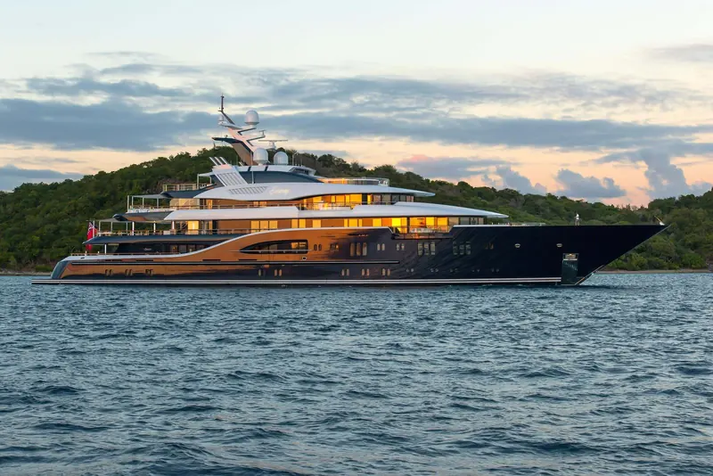 Solandge running at dusk with her name lit gold across the topsides, the low sheer and stepped superstructure Espen Oeino drew for the 80-metre Lurssen platform she shares with Ace and Quattroelle.