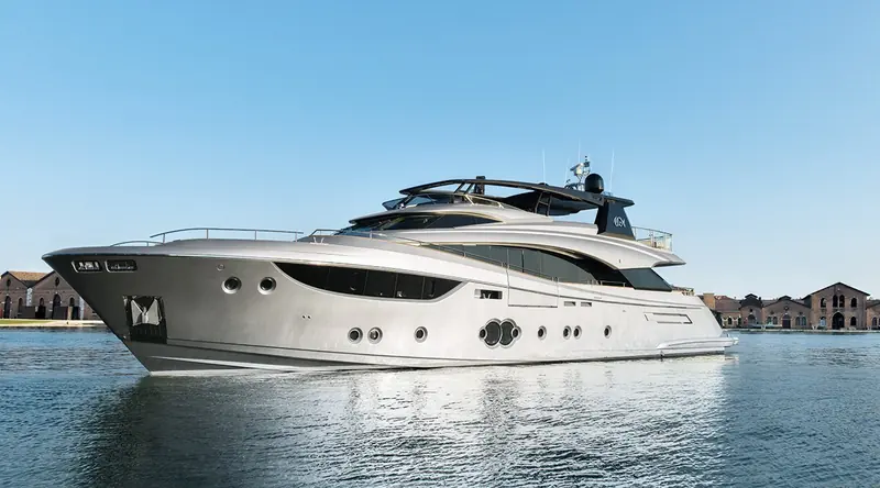 The MCY 105 idles past the redbrick warehouses of the Venice Arsenale in daylight, her sheer line and twin portholes glassy in the flat lagoon water.