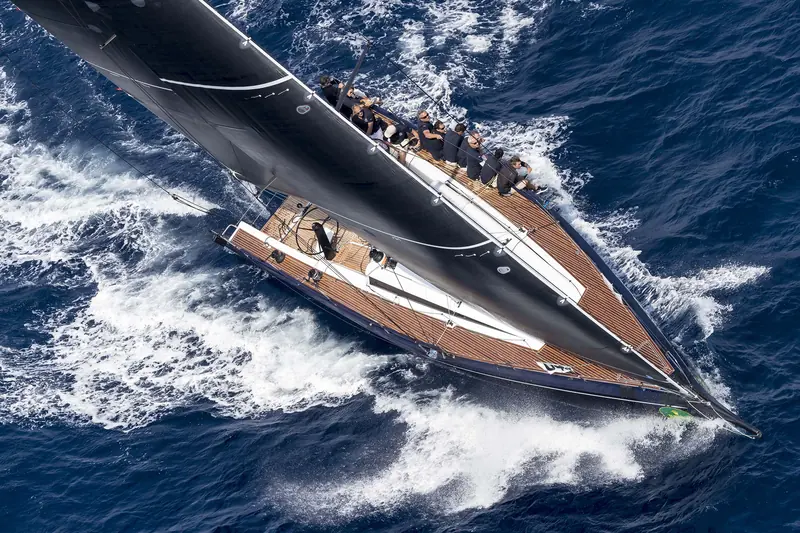 A ClubSwan 50 driving through a wave under full sail, crew hiked flat.