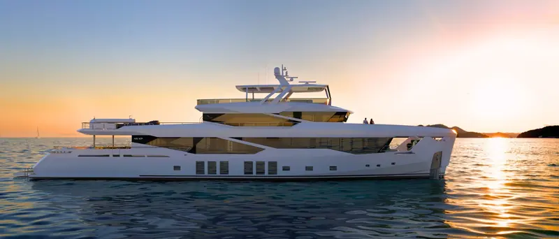 At anchor at sunset, guests visible on the flybridge - the open tender garage and drop-down bathing platform are folded away for the night.