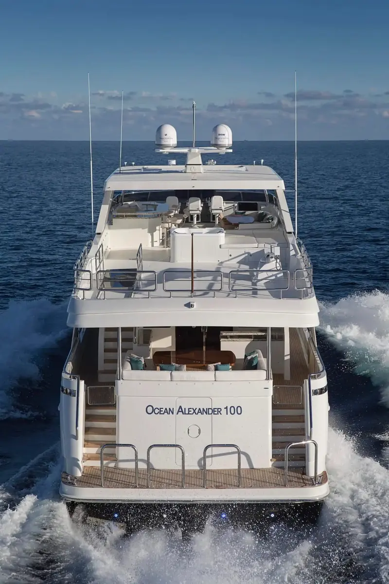 Stern-on at speed, the OCEAN ALEXANDER 100 nameplate legible on the transom above the swim platform and boarding stairs.