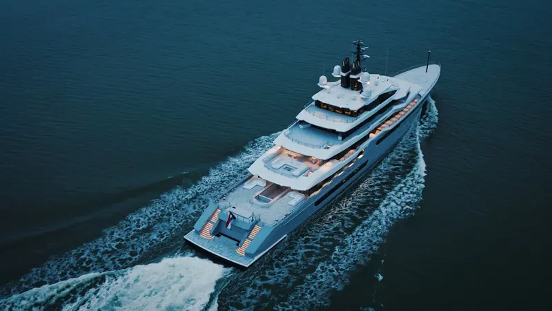 Running at dusk with the sundeck pool and stern platform lit, showing the aft-set helipad and the fold-down stern arrangement used for tender and dive-gear launching.