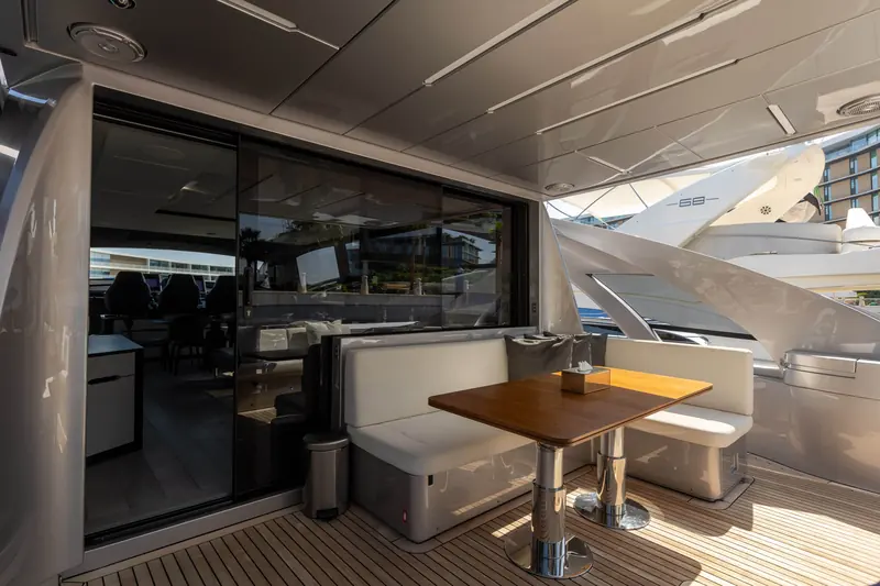 Aft cockpit dining table under the hardtop, with a second Pershing's flybridge visible in the marina behind.