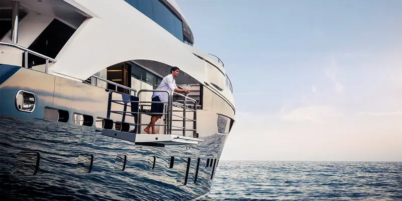 The starboard balcony off the owner's stateroom lowered open at sea, with the yacht's reflection running the length of the glossy topsides.