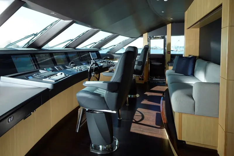 The raked wheelhouse windows and twin helm seats, with a dinghy dock and harbour visible through the glass.