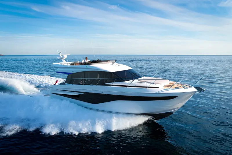 Running hard on a bright day, throwing a clean sheet of spray clear of the topsides rather than back over the side decks. Worth watching on a sea trial in a chop, since that is where a flybridge boat of this size either stays dry or does not.