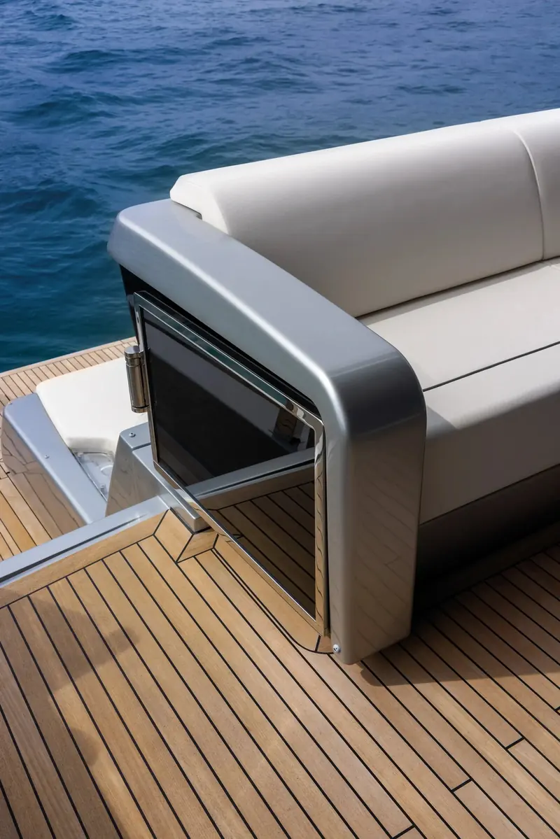 A corner sofa is built into the aft deck rail in polished steel and white leather, set directly onto the teak without a separate frame.