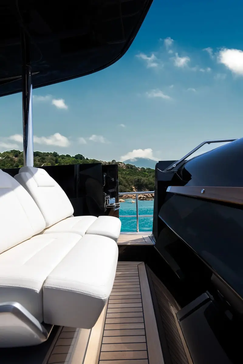 A private cove off Sardinia's coast reflected in the transom glass, with the sunpad and locker doors of the beach club aft.